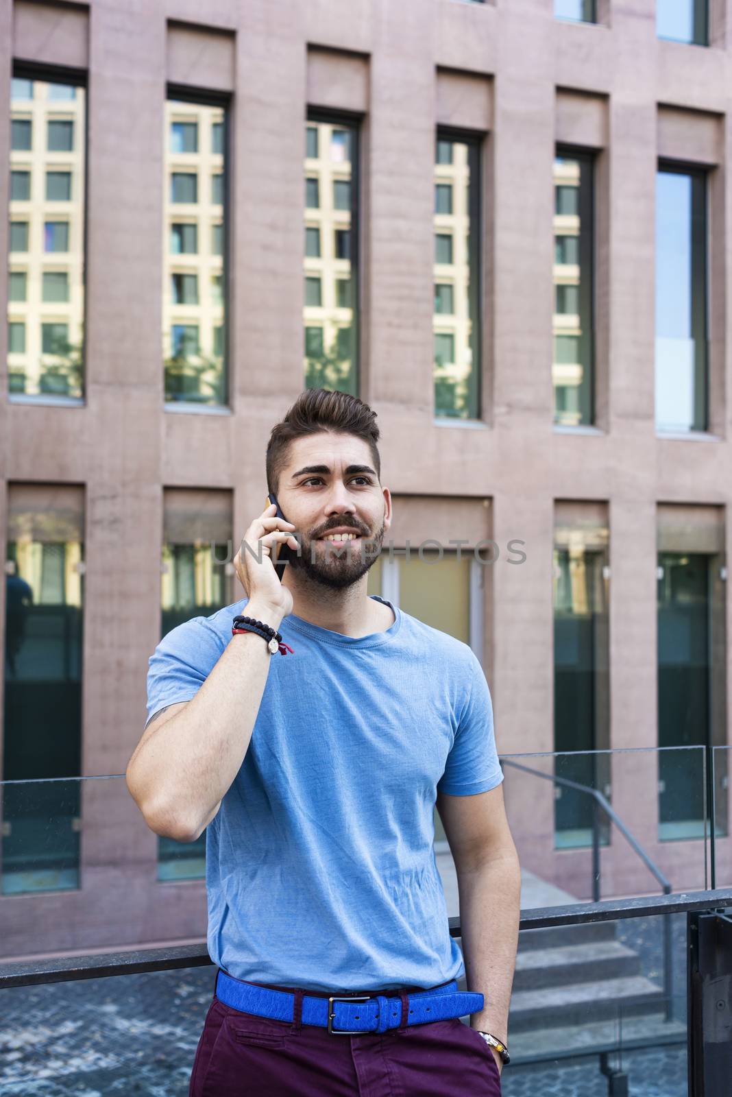 Portrait of cheerful modern businessman speaking by phone and smiling while standing outdoors