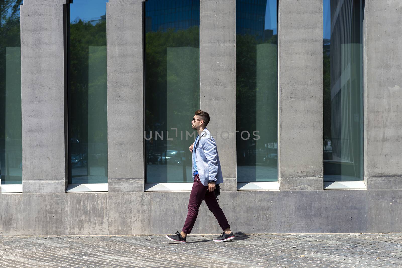 Young businessman walking next to office buildings while holding a shoulder bag outdoors