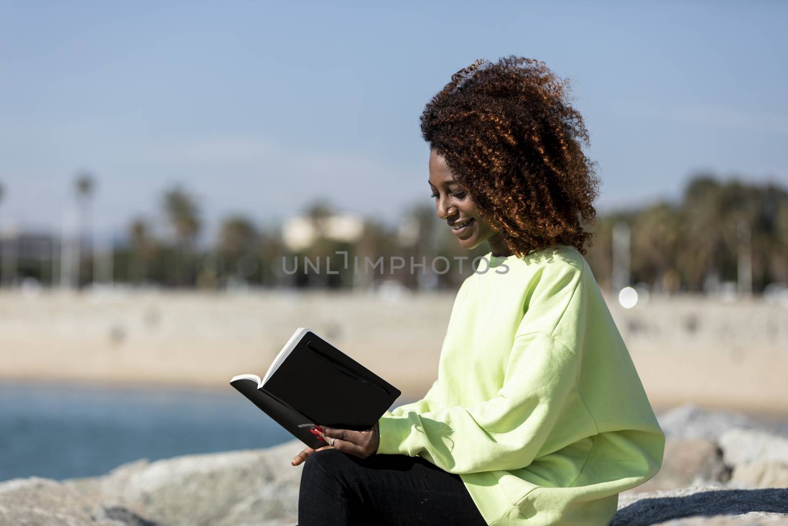 afro american woman sitting on shore while reading a book in a sunny day