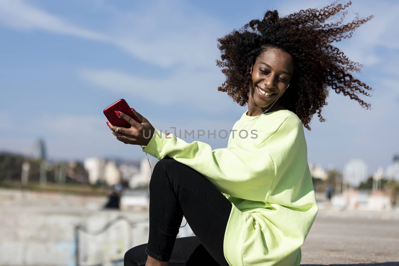 Afro american woman sitting on shore using a mobile phone in a sunny day