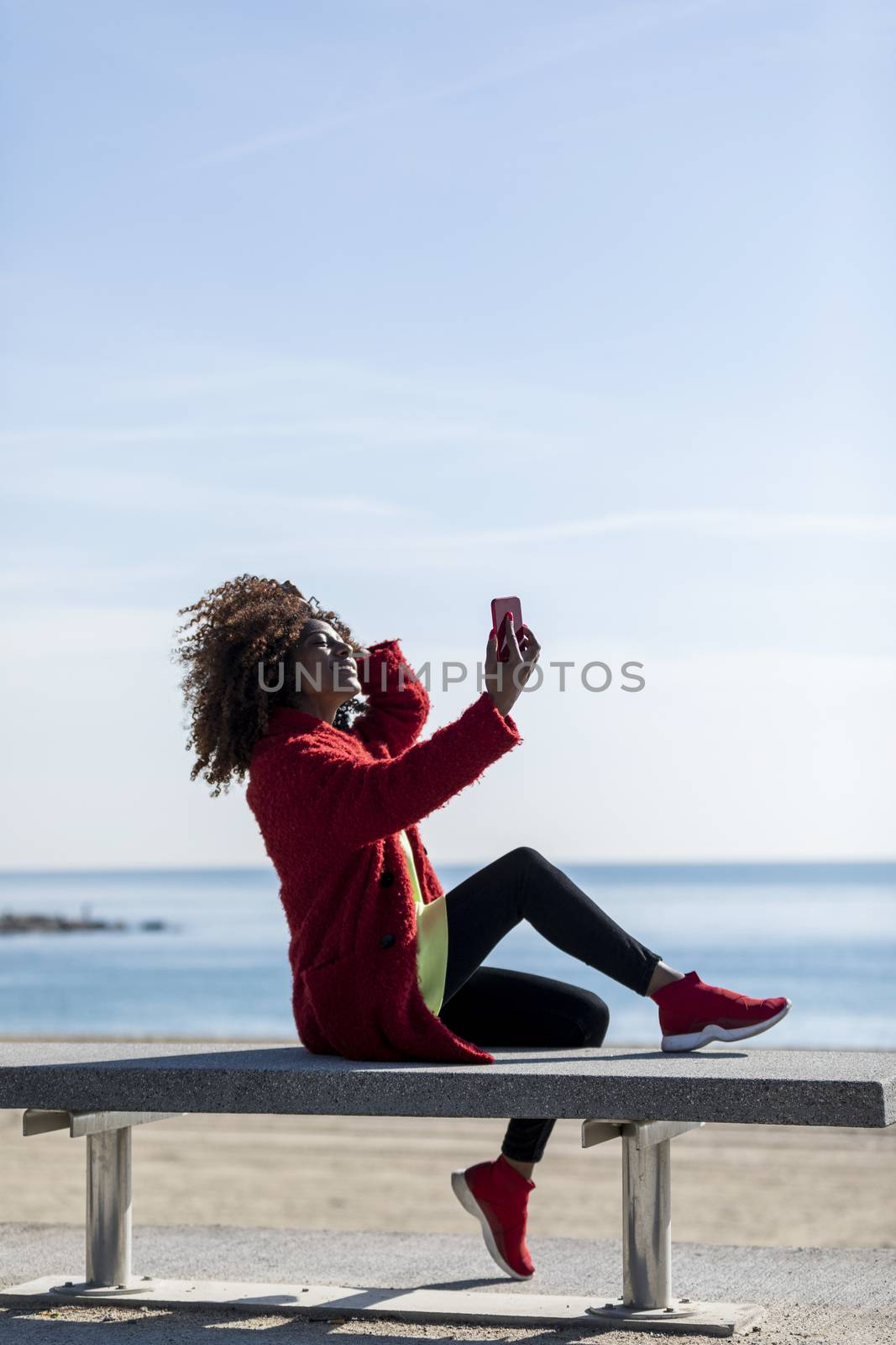 Afro american woman sitting on shore using a mobile phone in a sunny day