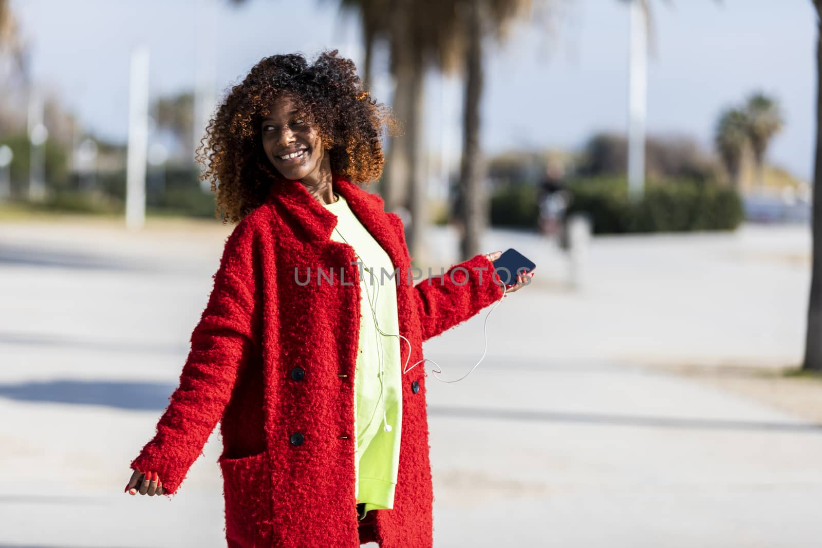 Young afro american woman laughing while dancing outdoors with red jacket