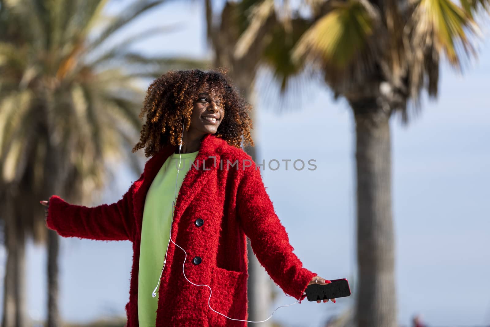 Young afro american woman laughing while dancing outdoors with red jacket