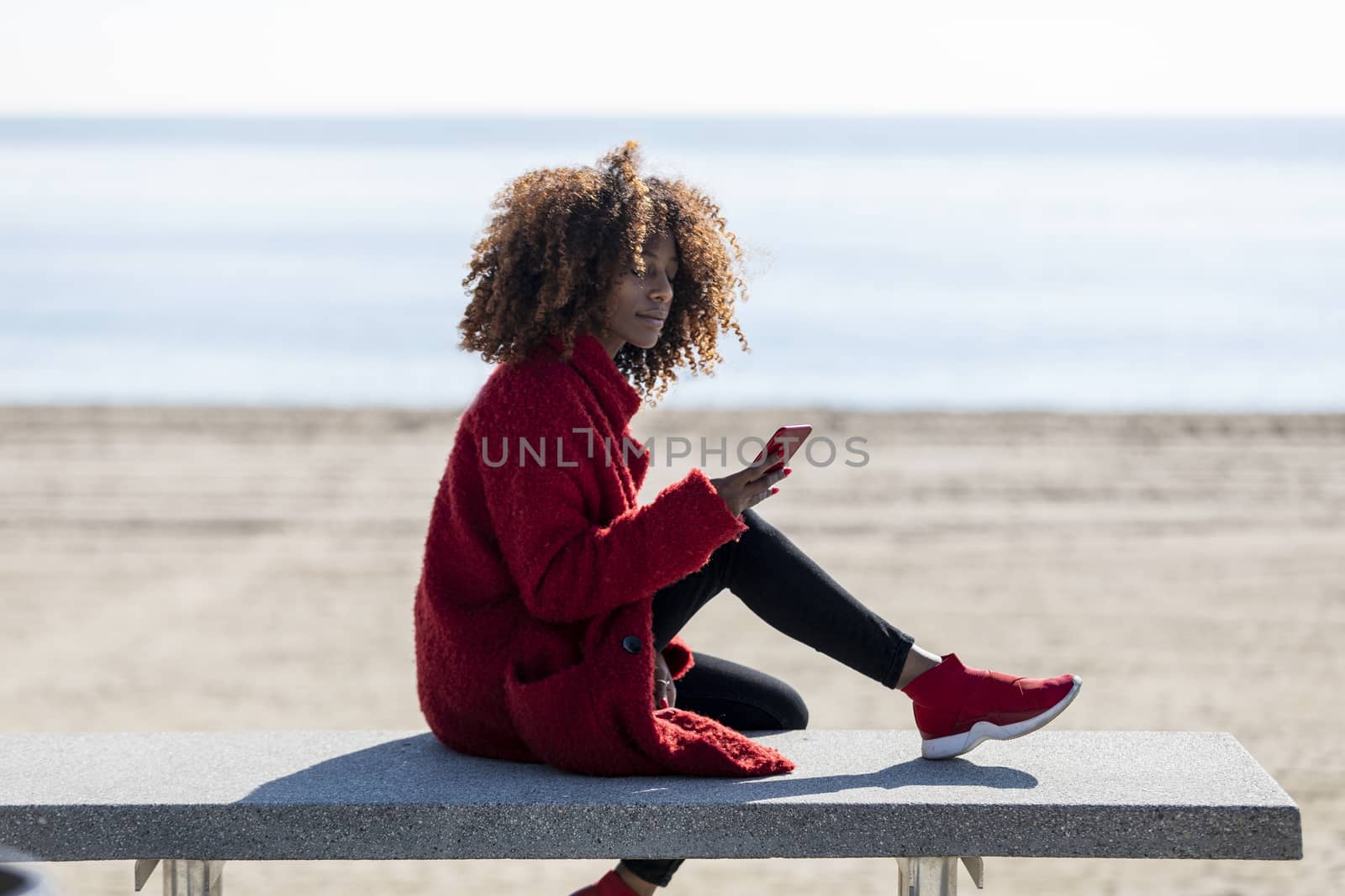 Afro american woman sitting on shore using a mobile phone in a sunny day