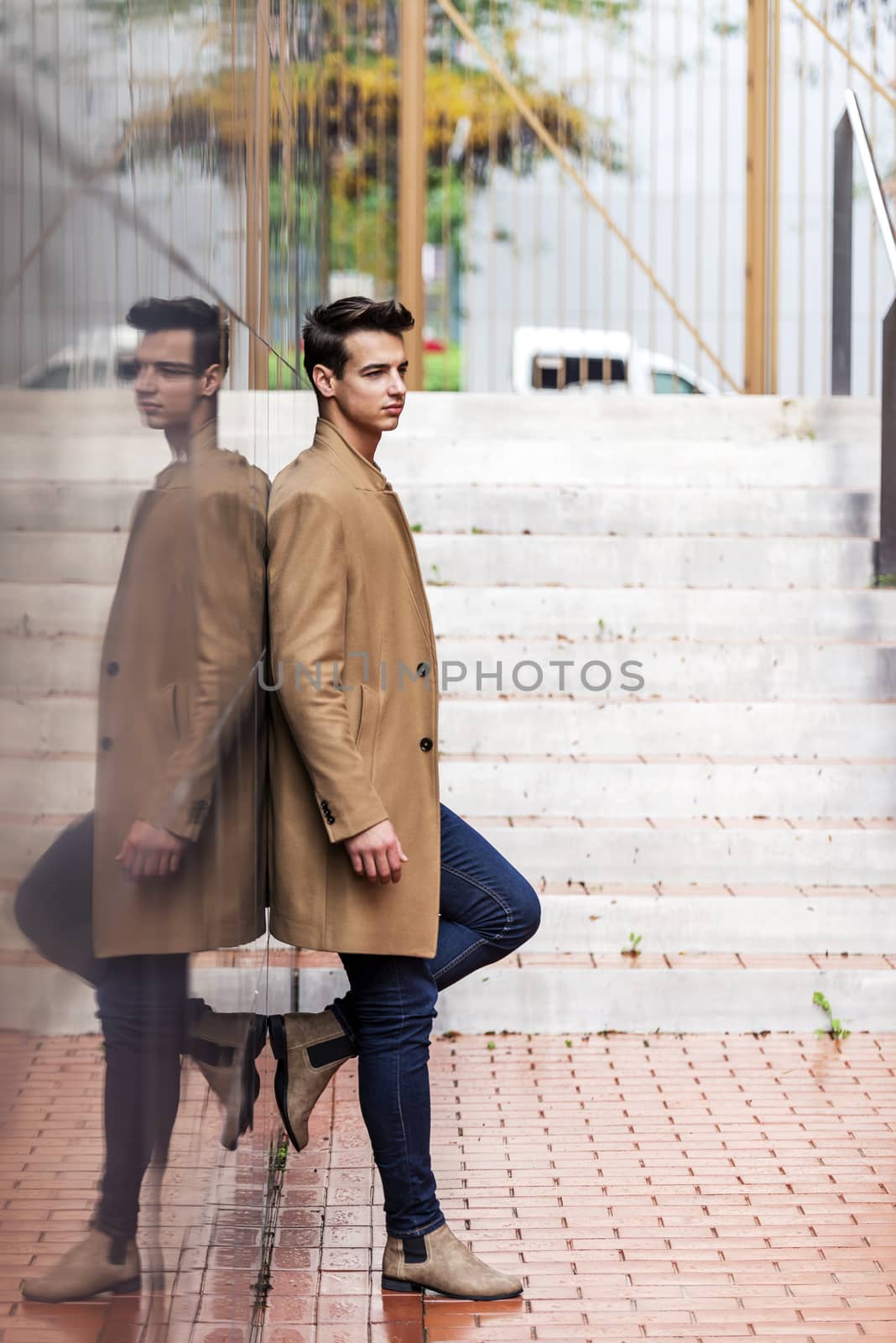 Side view of young stylish man leaning on black wall while looking away outdoors in sunny day