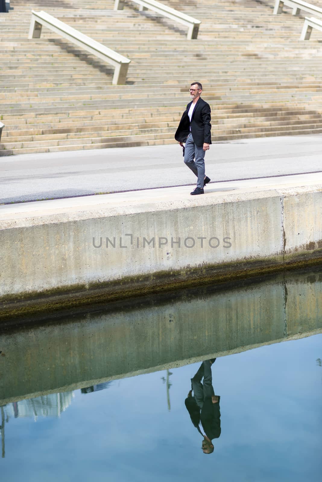 Adult man in formal clothes while walking on promenade holding an umbrella.