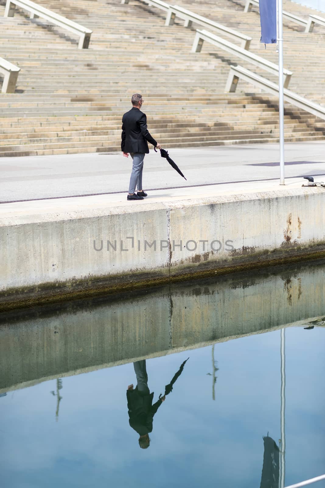 Adult man wearing formal clothes while walking on promenade holding an umbrella. by raferto1973