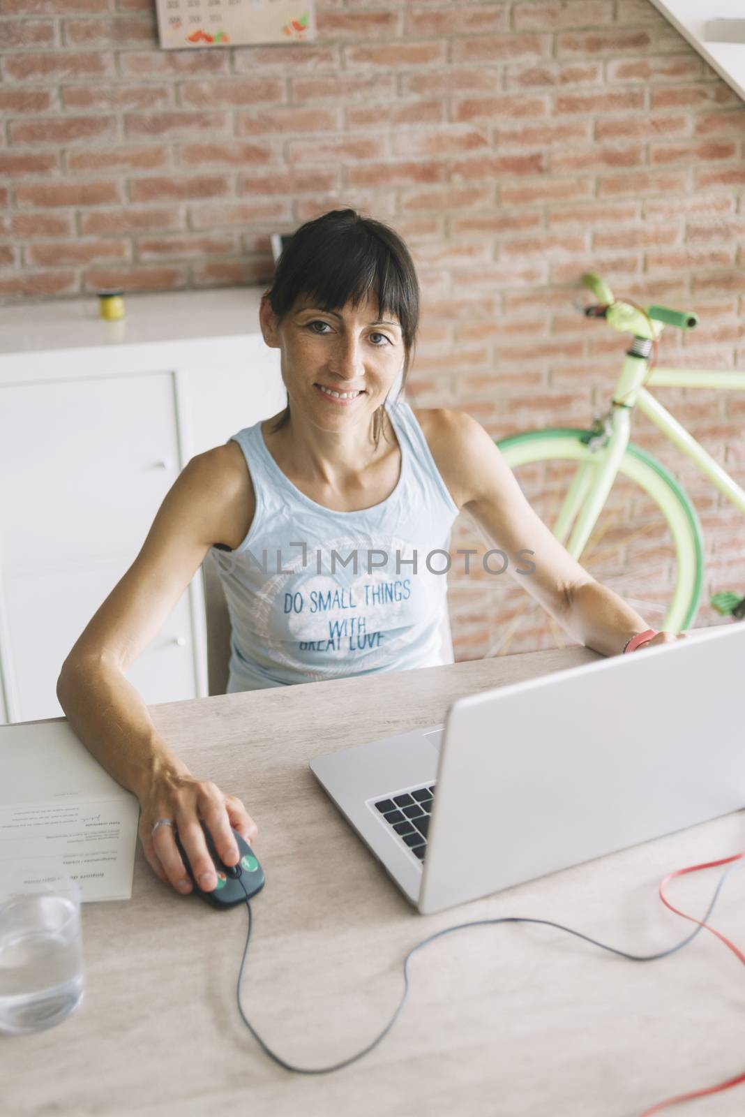 Smiling woman with laptop working at home while looking camera by raferto1973