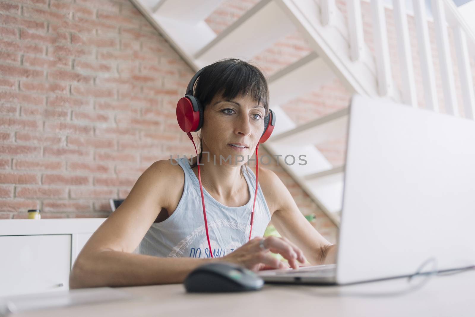 Woman with laptop working at home while listening music by headphones
