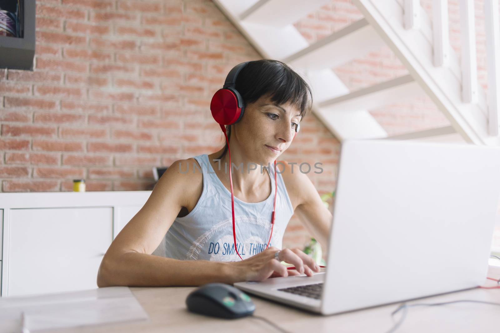 Woman with laptop working at home while listening music by headphones