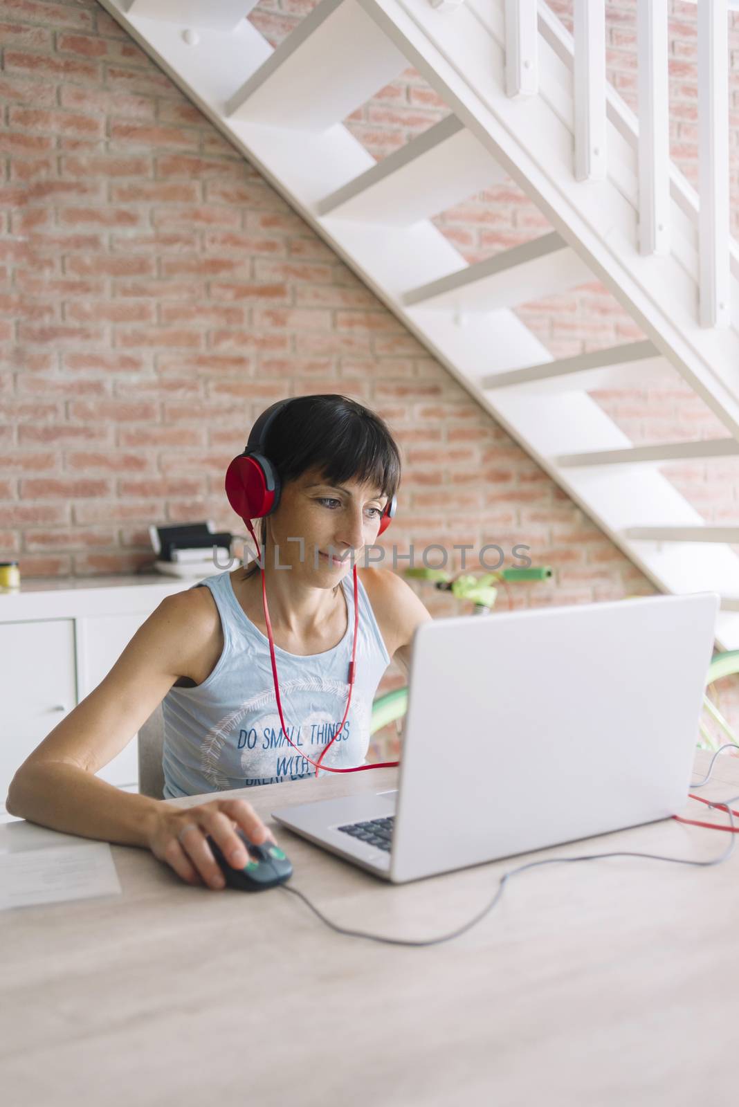 Woman with laptop working at home while listening music by headphones