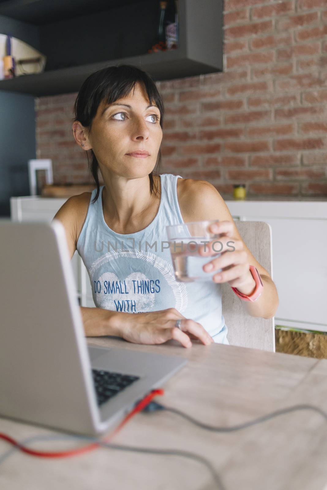 Woman with laptop working at home while holding a glass of fresh by raferto1973