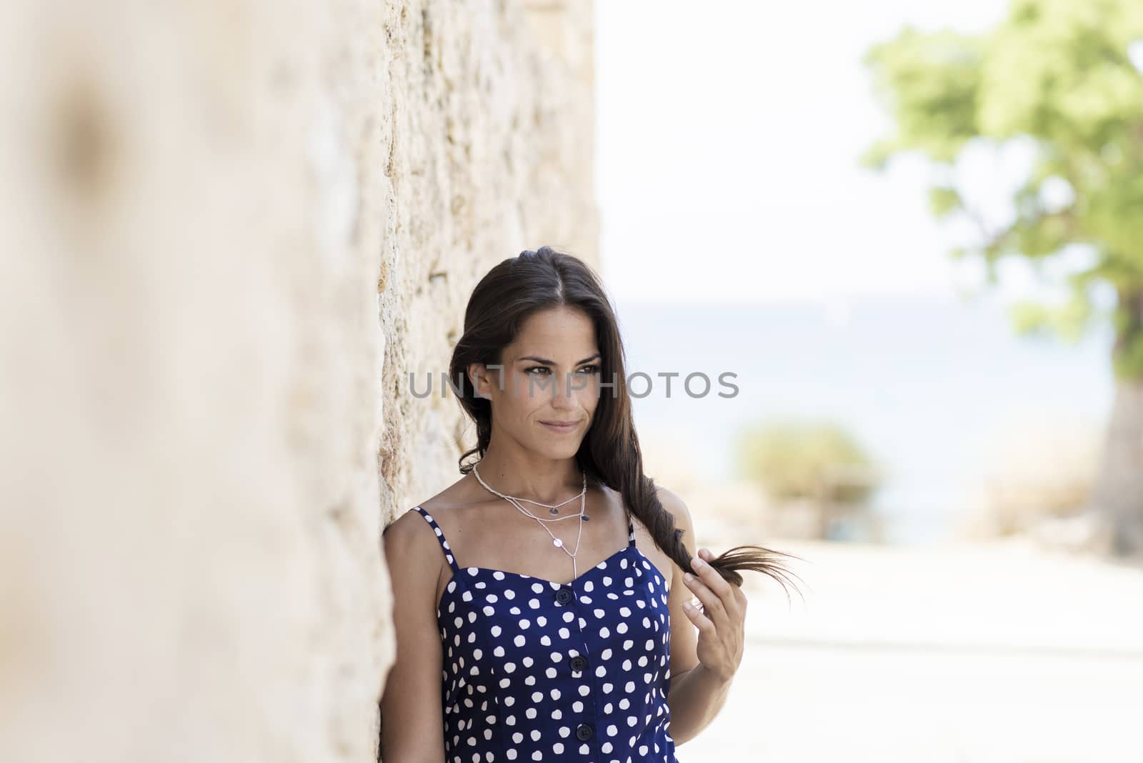 Beautiful smiling woman in blue dress leaning on wall while looking away