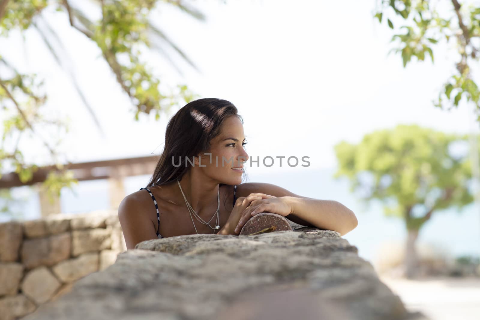 Beautiful smiling woman in blue dress leaning on wall while looking away