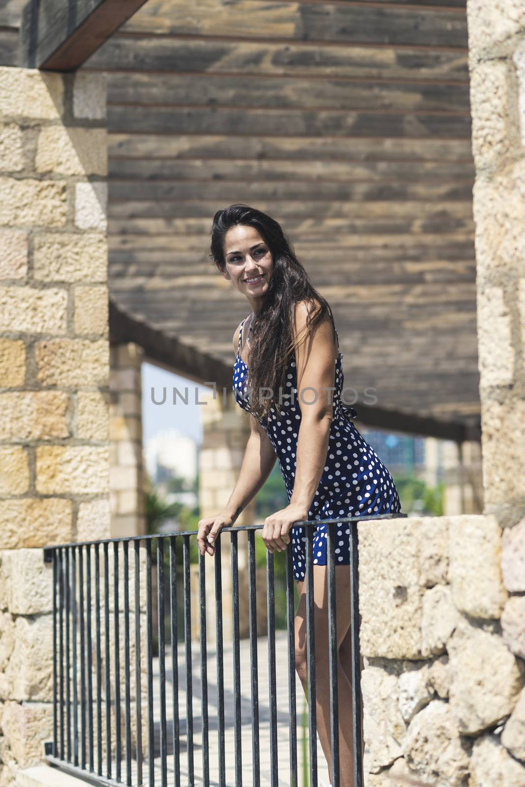 Beautiful smiling woman in blue dress leaning on fence while looking away