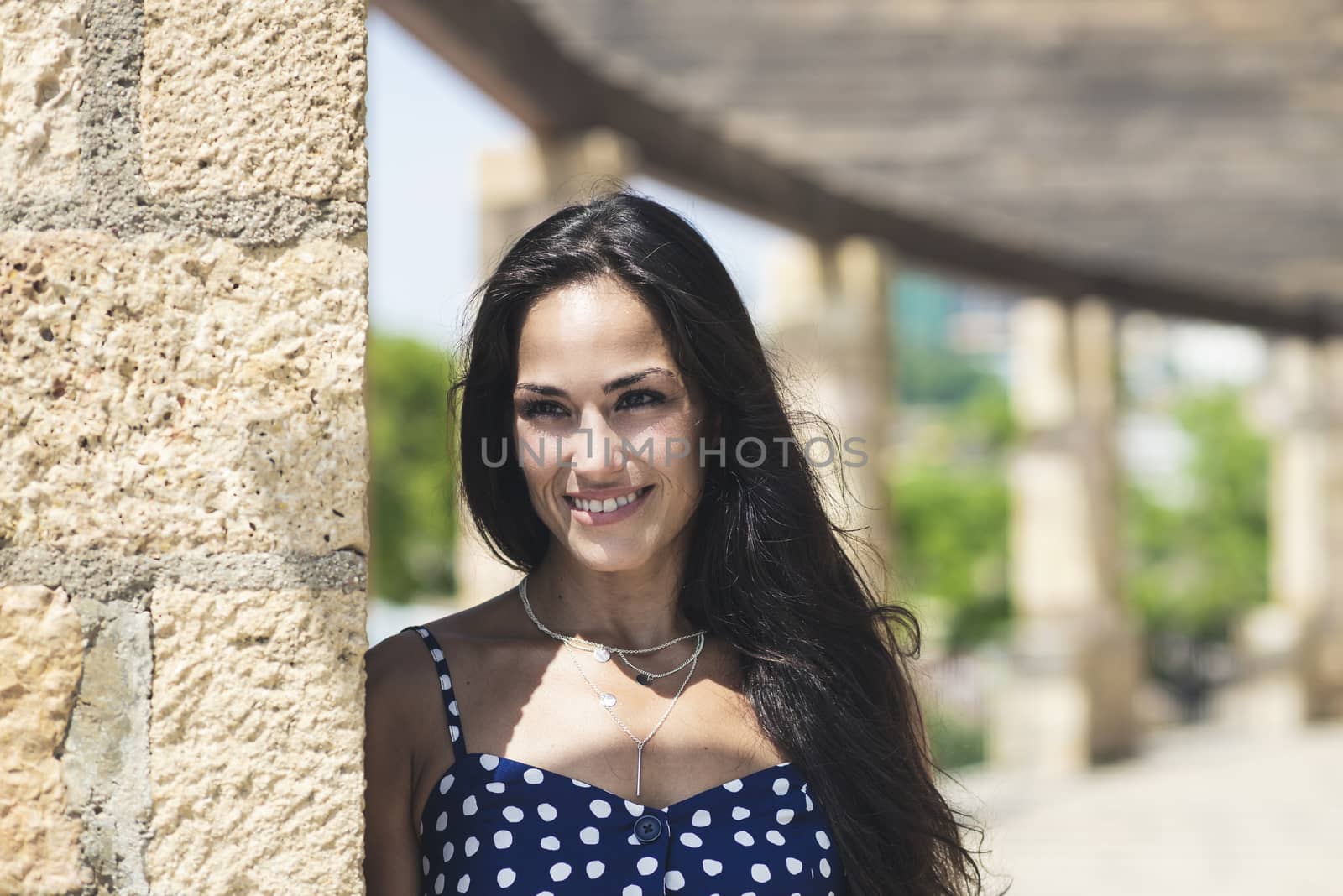 Beautiful smiling woman in blue dress leaning on wall while looking away