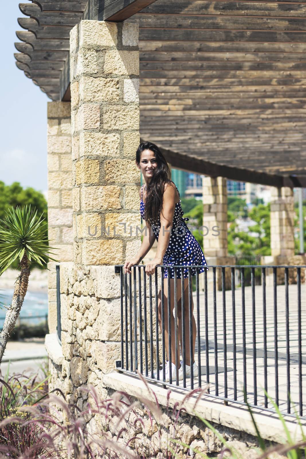 Beautiful smiling woman in blue dress leaning on fence while looking away