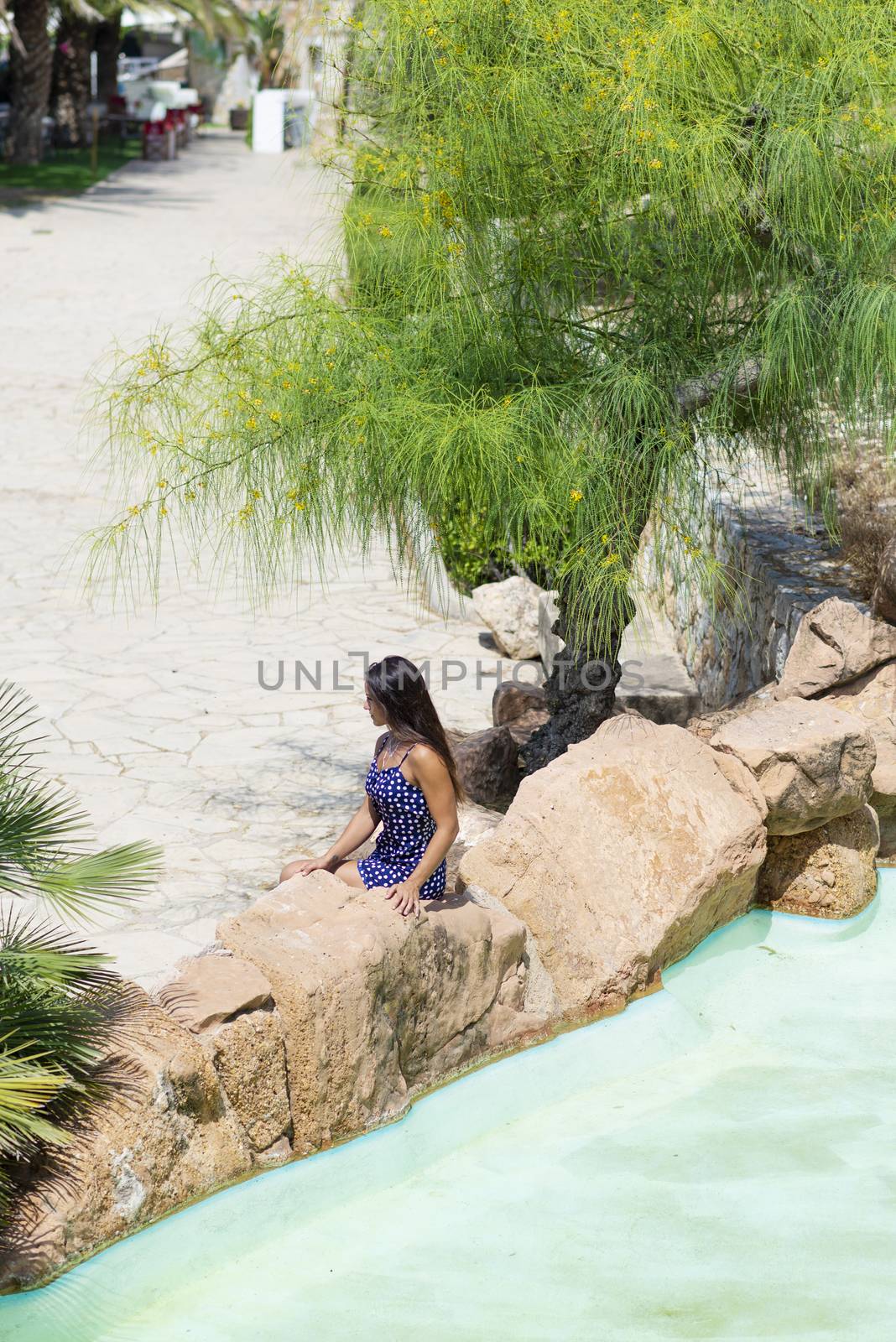 Top view of a pretty young hispanic woman sitting on rock next to a water pond