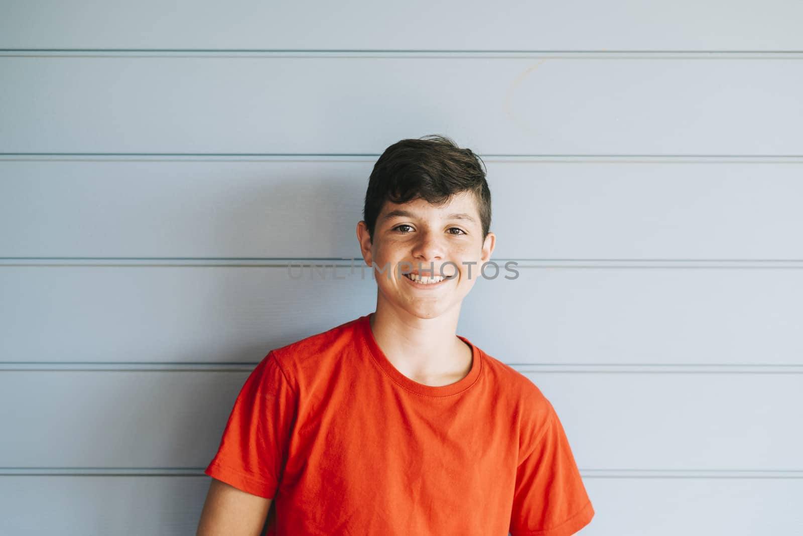 Portrait of a cheerful male teen leaning on wood wall while looking camera in a sunny day