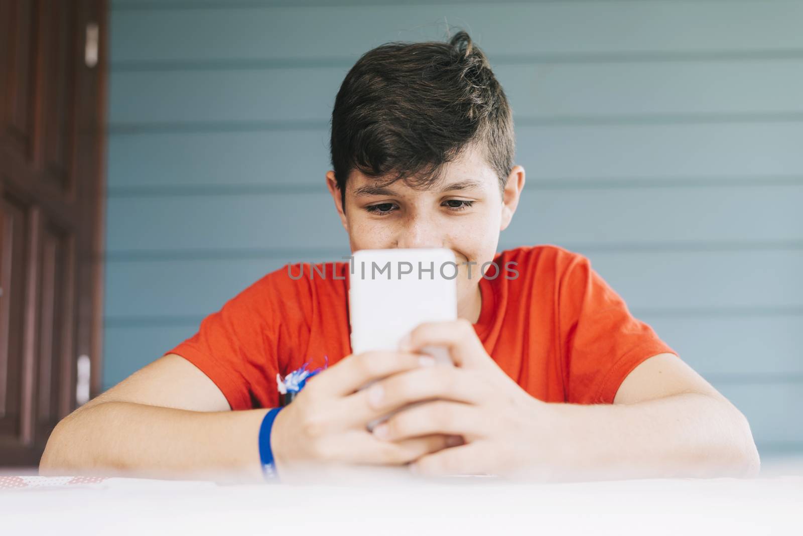 Handsome Caucasian 13-year old boy wearing red t-shirt sitting outdoors using electronic gadget by raferto1973