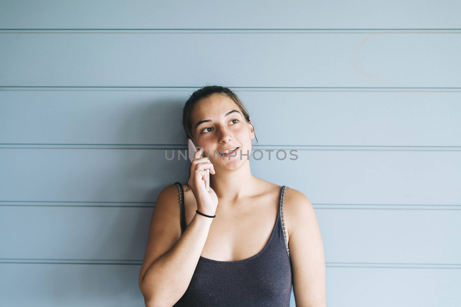 Attractive young adult female in summer dress talking on cell phone while leaning against wood paneled wall