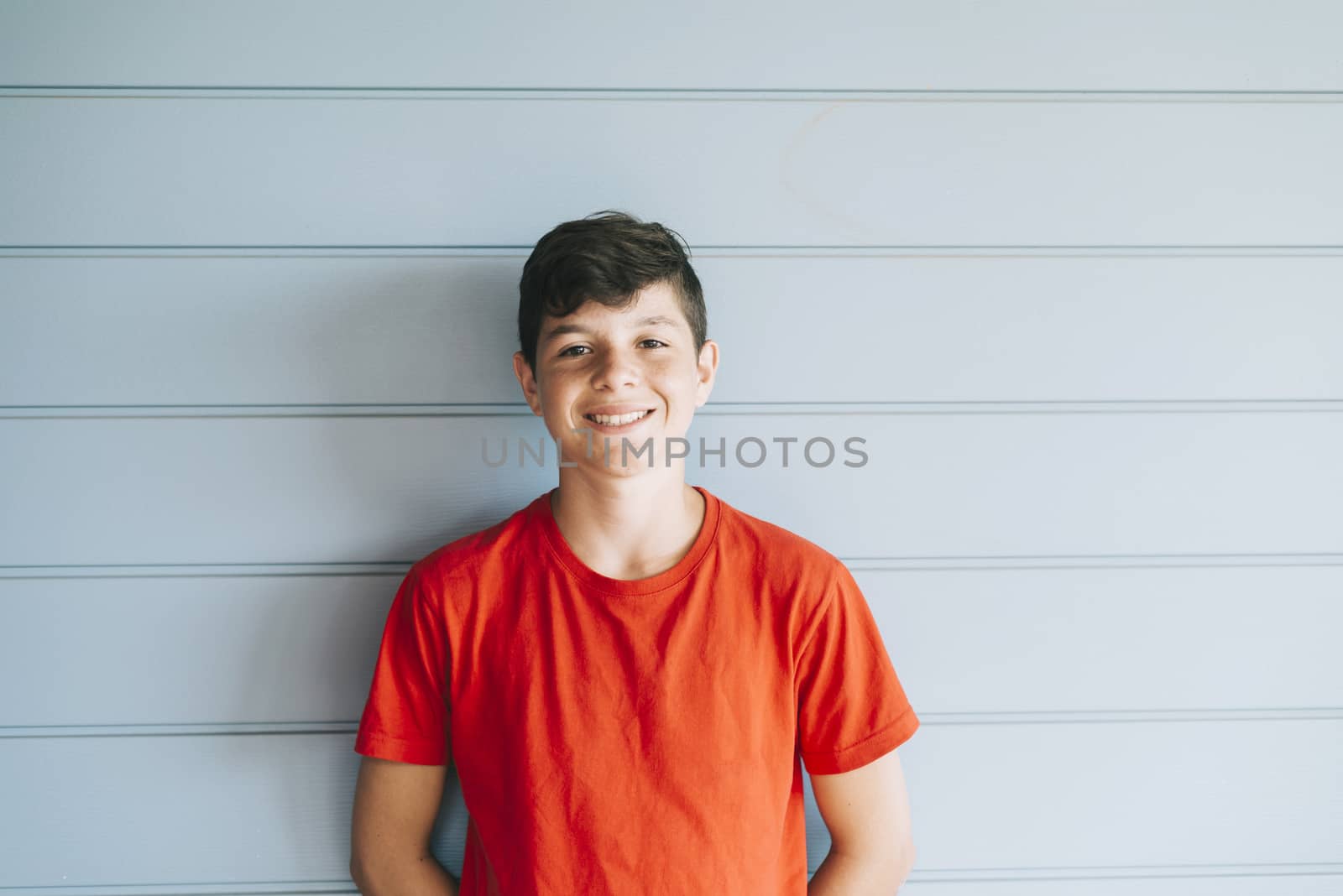 Portrait of a cheerful male teen leaning on wood wall while looking camera in a sunny day