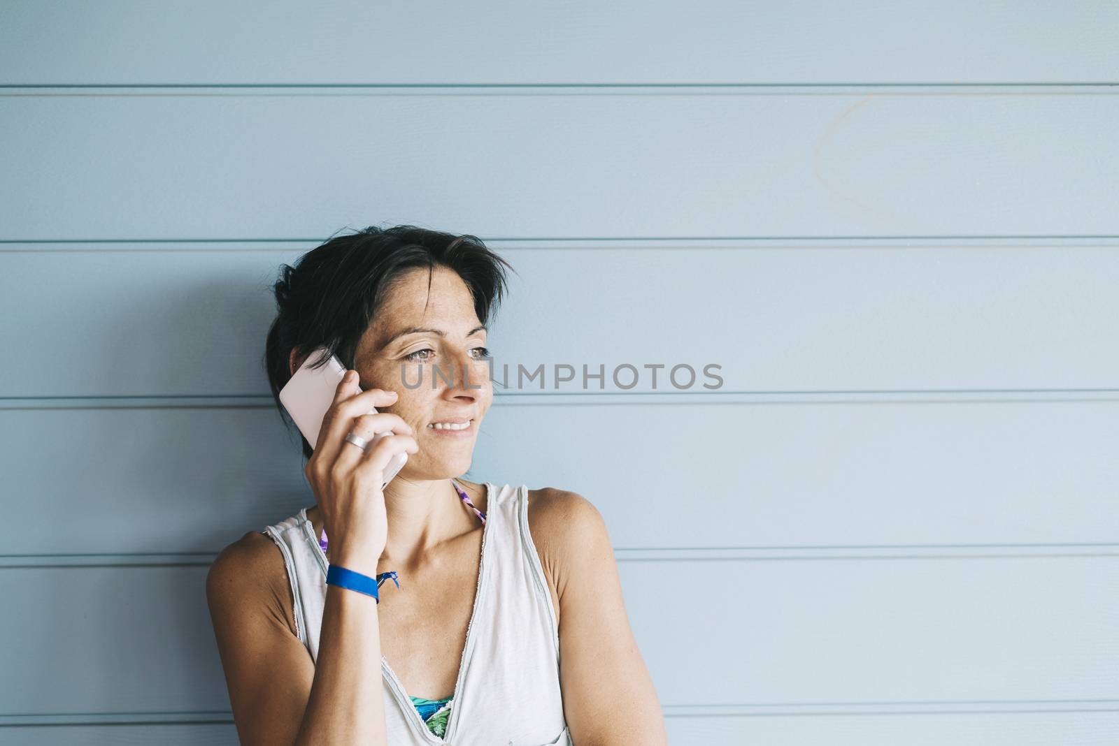 Young adult female in summer dress talking on cell phone while leaning against wood paneled wall by raferto1973