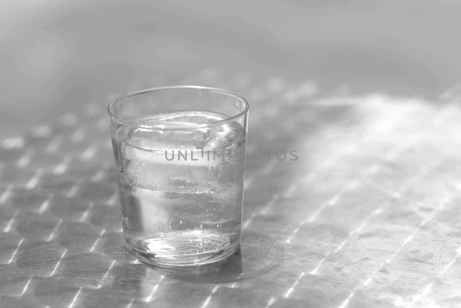 Glass of water with ice on a metallic table outdoors in a bright day