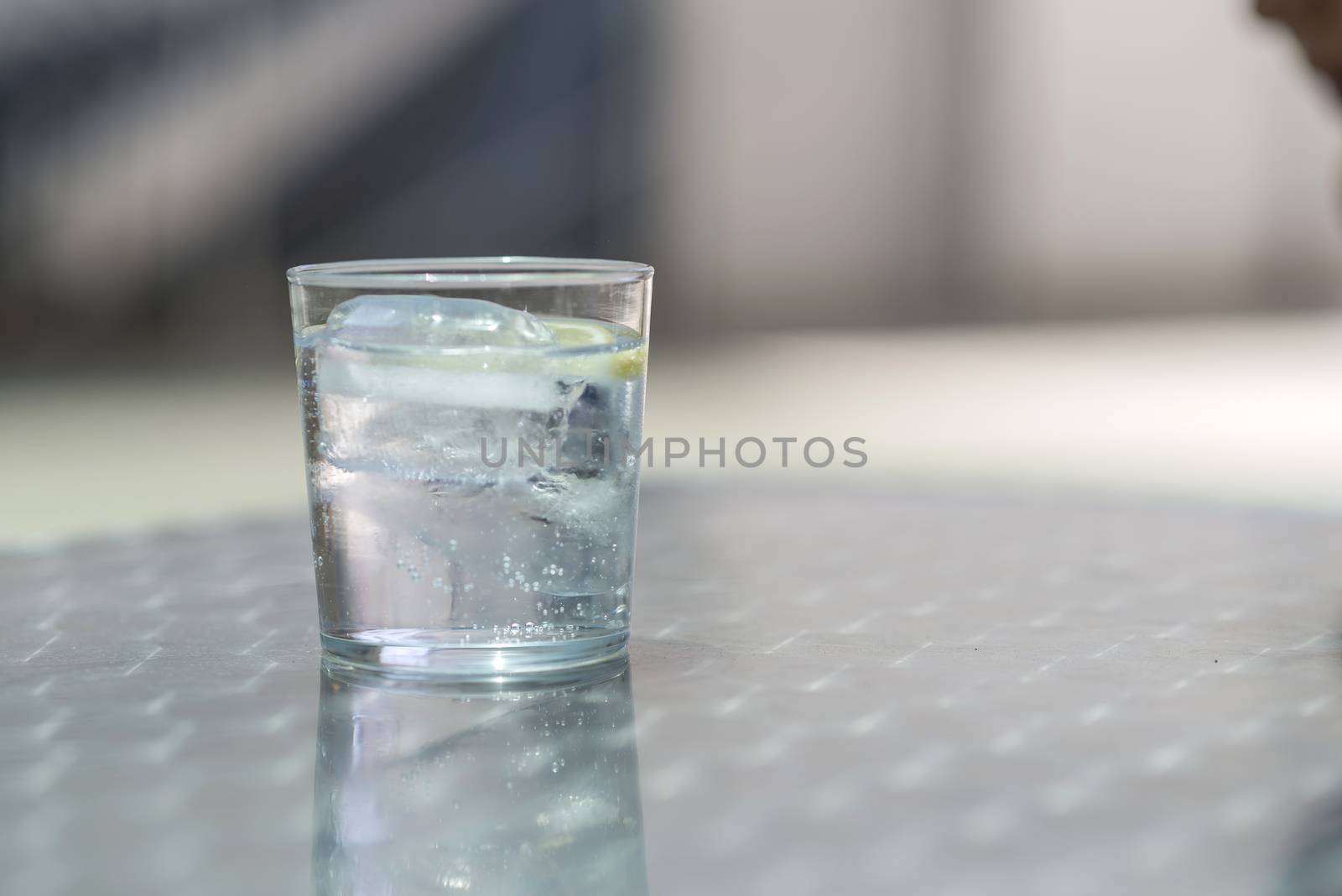 Glass of water with ice on a metallic table outdoors in a bright day