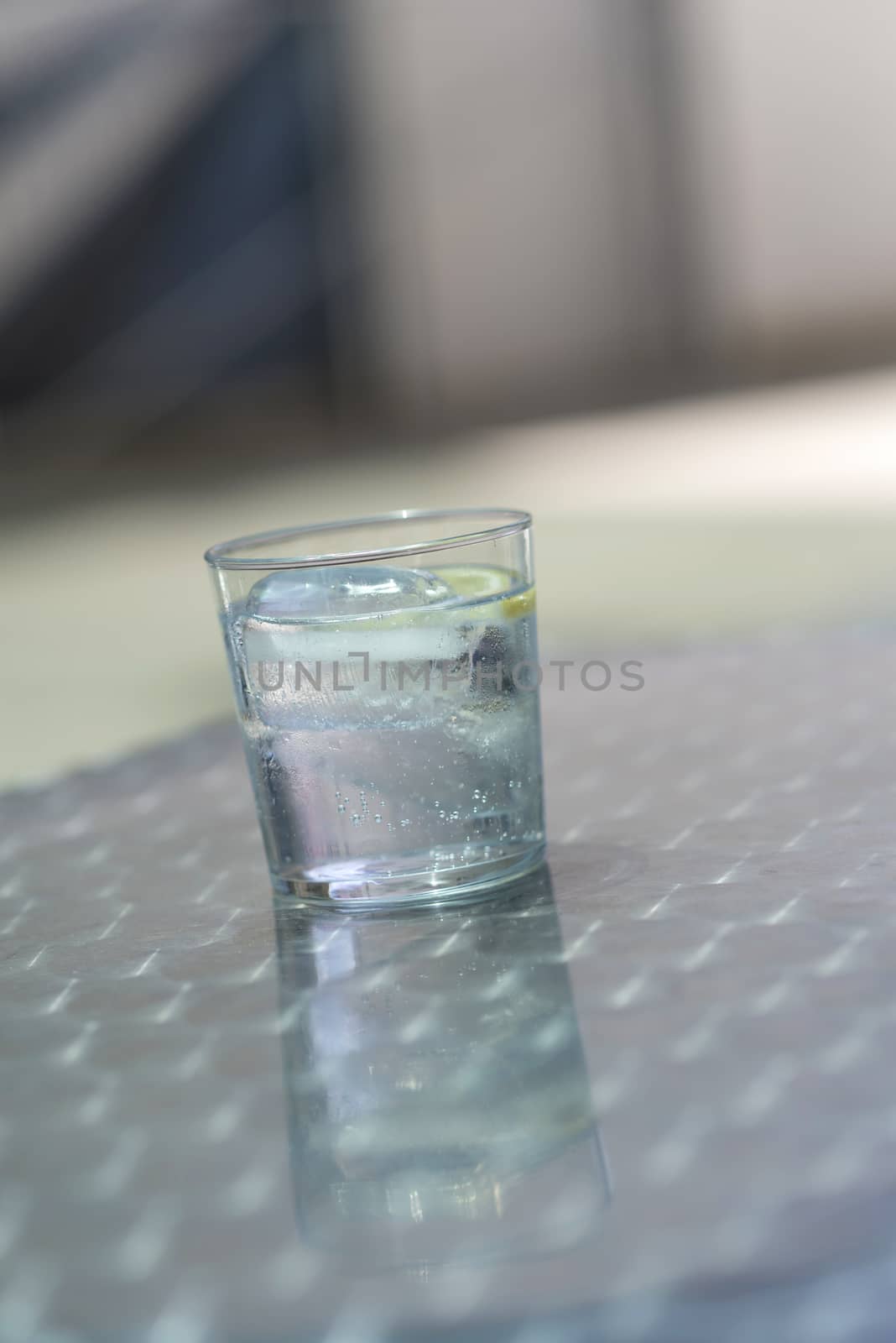 Glass of water with ice on a metallic table outdoors in a bright day