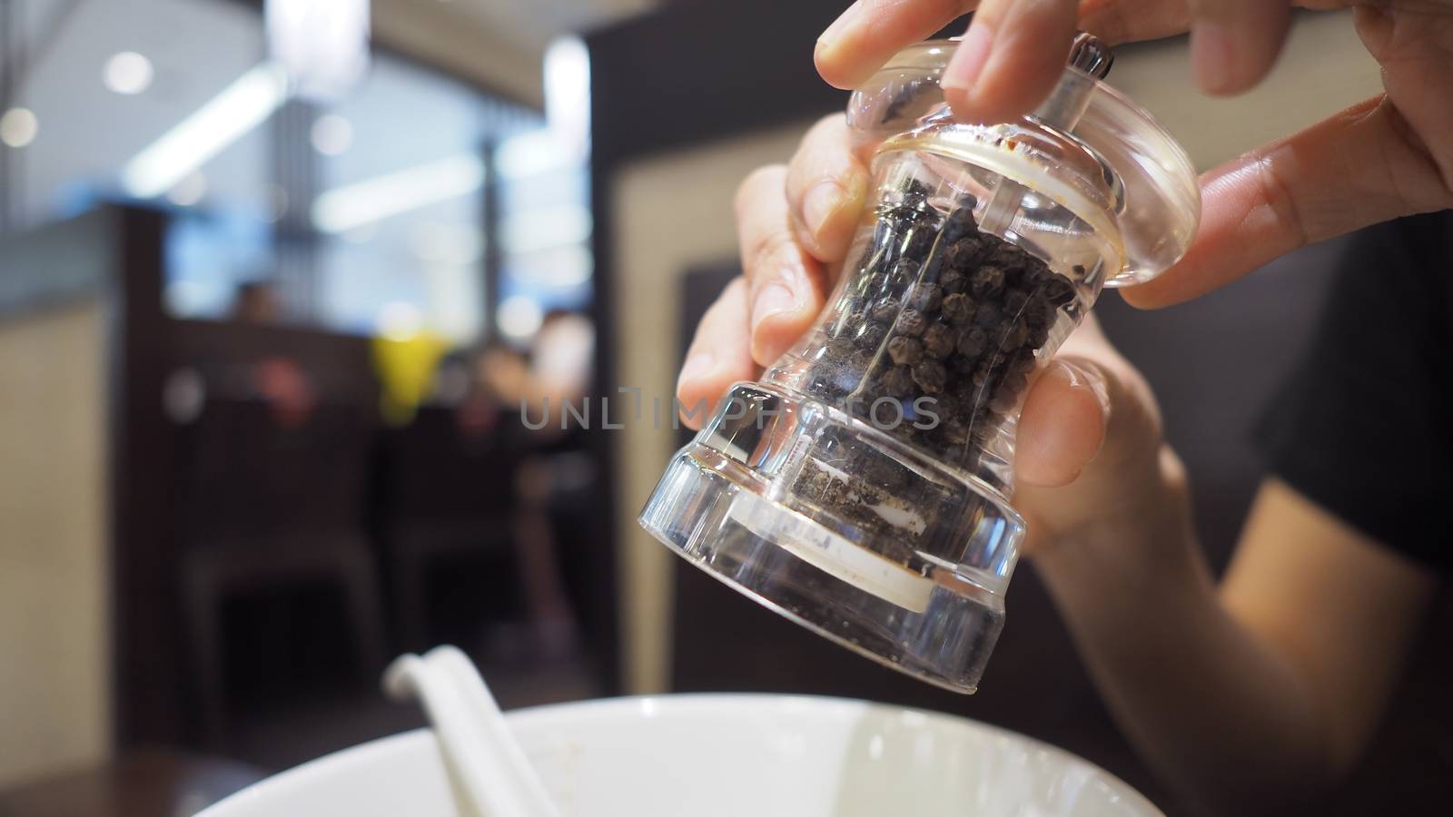 Clear color glass and Thailand black pepper mill or grinder in hands that twisting the bottle and pouring or adding small pieces of spices to plate or bowl for a better taste in the meal.