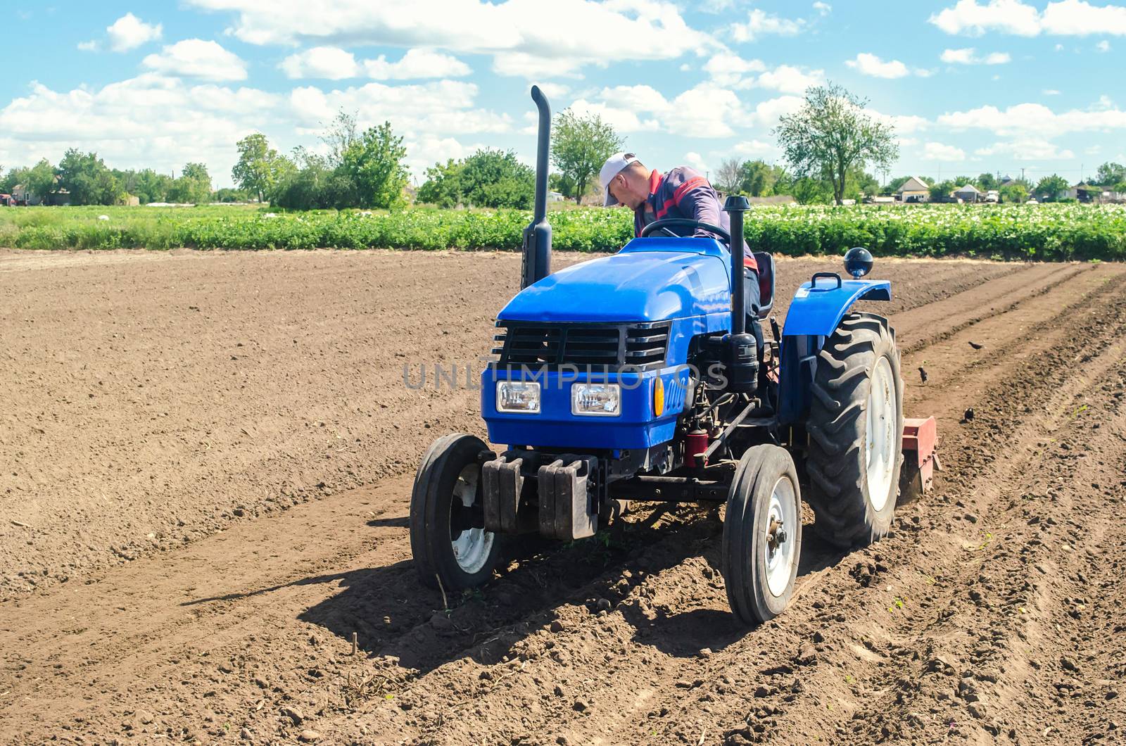 Farmer on a tractor loosens the soil with milling equipment. Loosening surface, land cultivation. Farming, agriculture. Plowing field. Use of agricultural machinery and to simplify and speed up work. by iLixe48