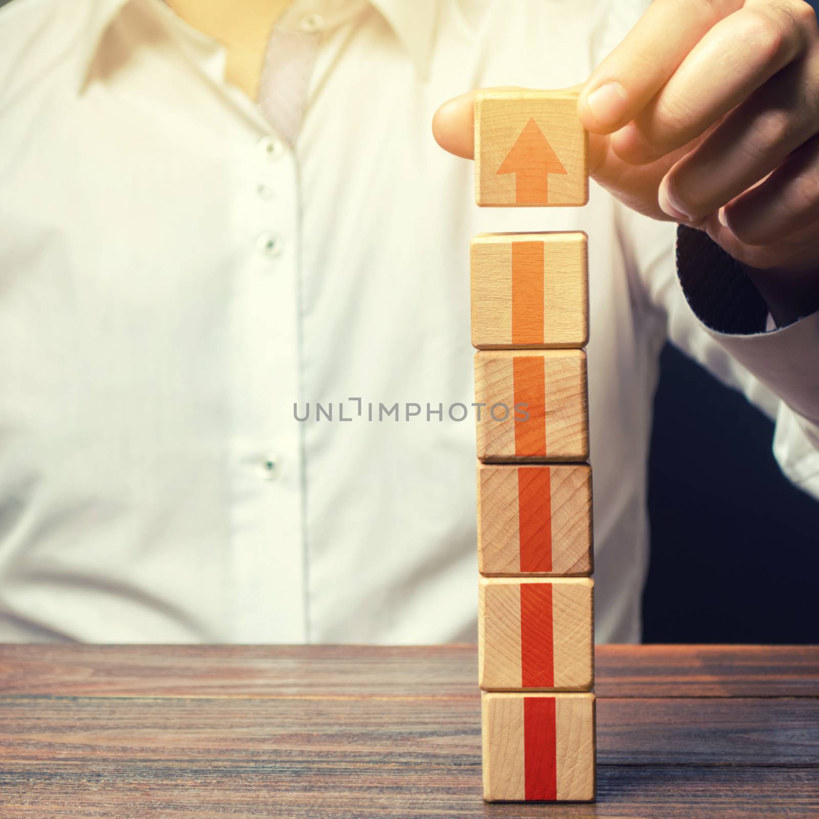 Businessman builds a tower of blocks with an up arrow. Career promotion, growth of professional skills. Profit growth. Marketing. Improving efficiency. Business development, expansion improvement.