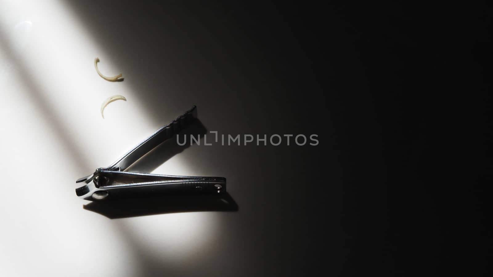 Close-up images of nail clipper from top view angle after cut out sensitive damage nails from hands and fingers and lay down on the floor and have sun light shade and shadow on it.