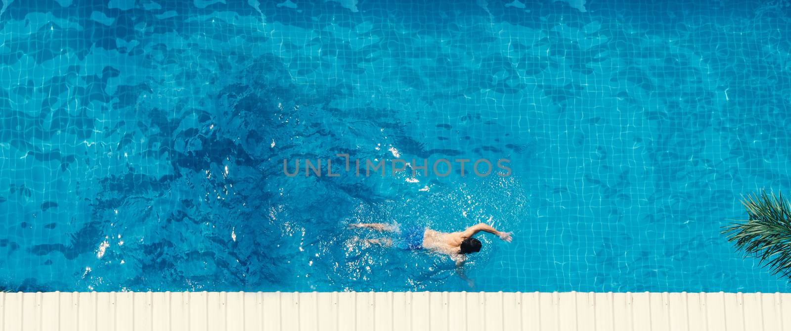 Swimming pool top view angle which young man relaxing and enjoying in pools of his hotel in summer season of Thailand at vacation day and have sun light and flares on blue water surface.