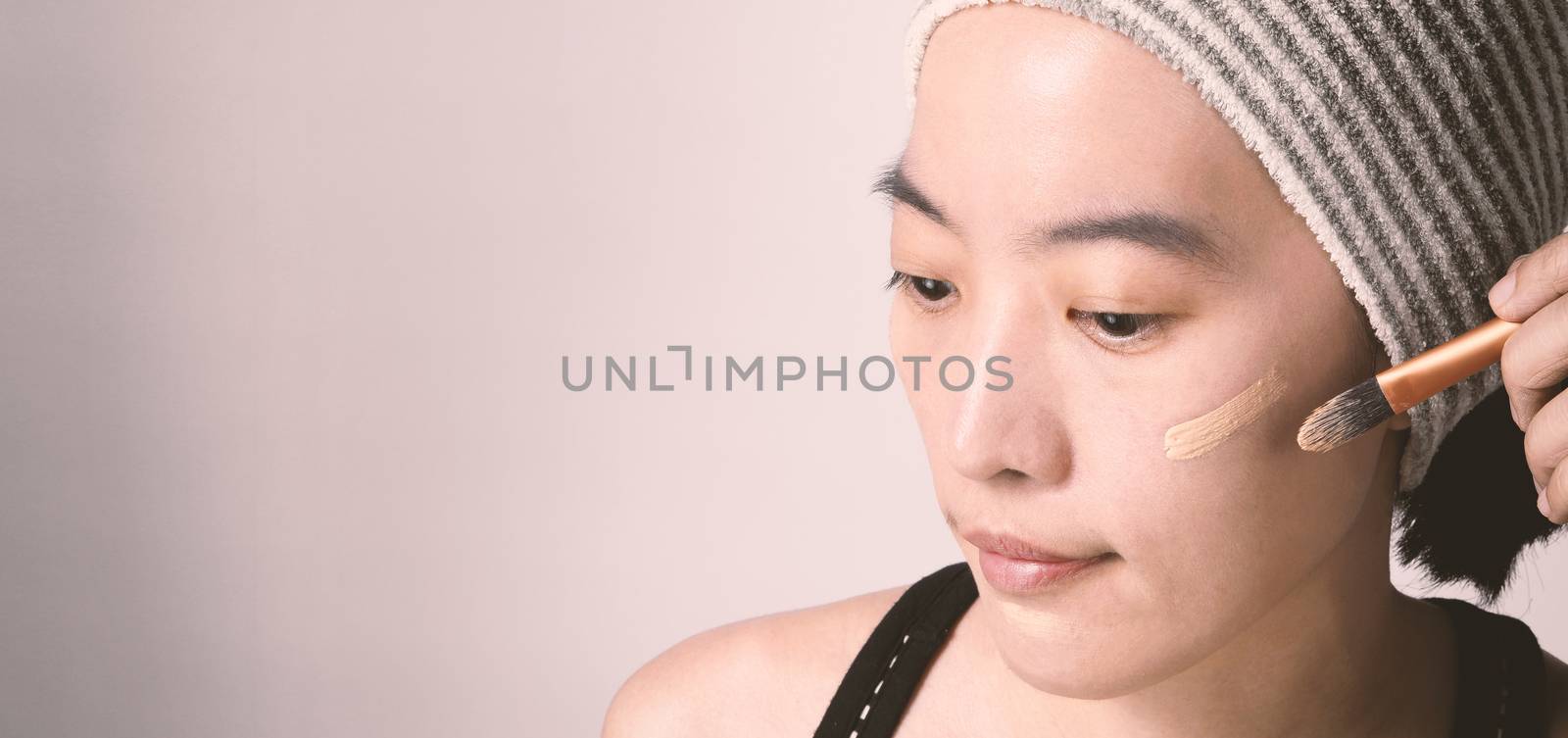 Asian girl or woman 40 years old beautiful face with japanese look making up by foundation liquid and cosmetic brush on sensitive skin for helping her complexion look flawless and no retouch.