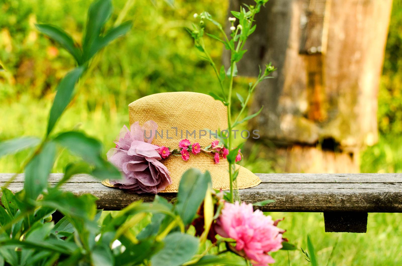 Straw hat with pink flowers on a wooden fence