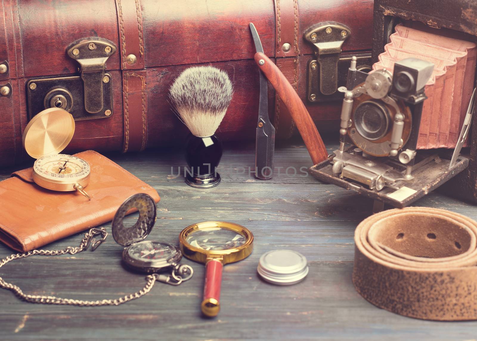 old fashioned objects brush, suitcase, compass, razor, watch, old camera, magnifying glass, balsam, leather belt on a wooden background