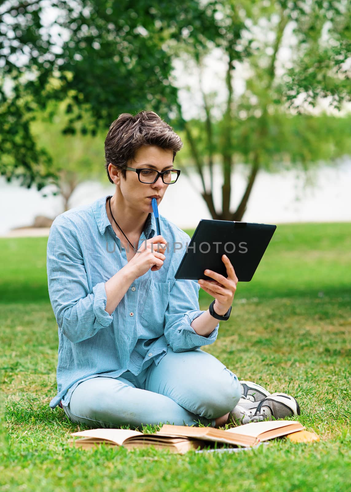 Woman sitting on green grass and studying online on tablet
