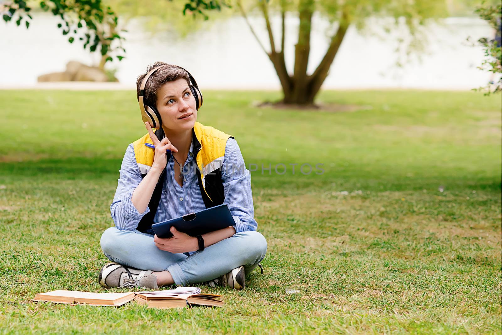 Woman in headphones sitting on green grass and studying online on tablet