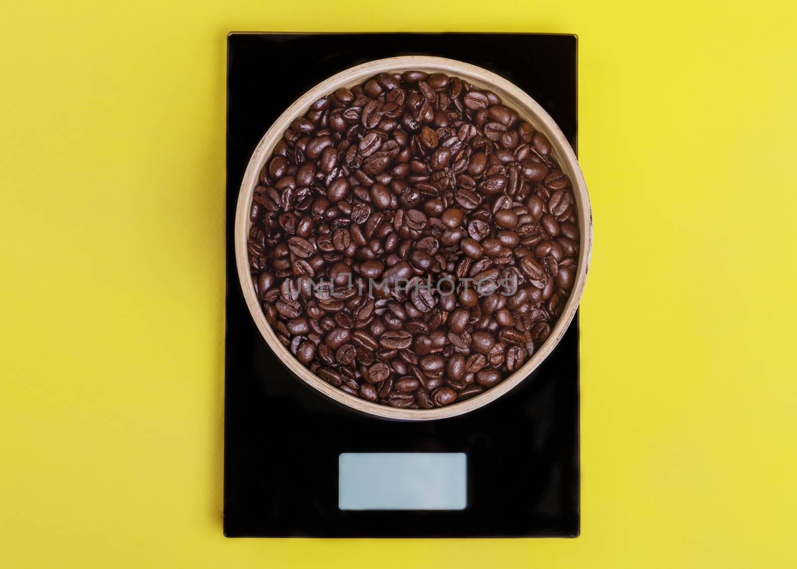 Wooden bowl with coffee beans on black scales on the yellow background.