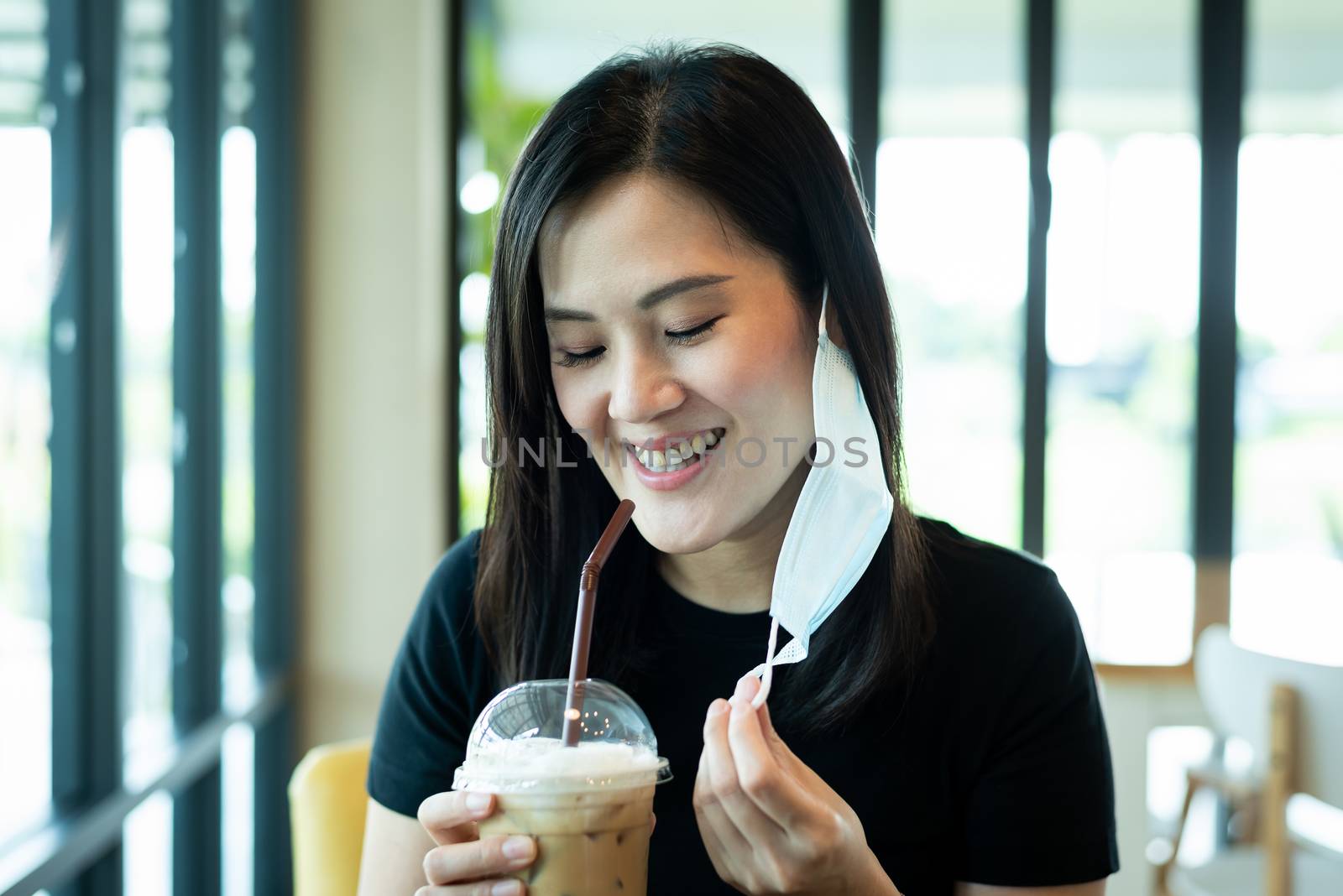 An Asian beautiful woman has to remove a blue mask and drinking an iced cappuccino with happiness in the morning.