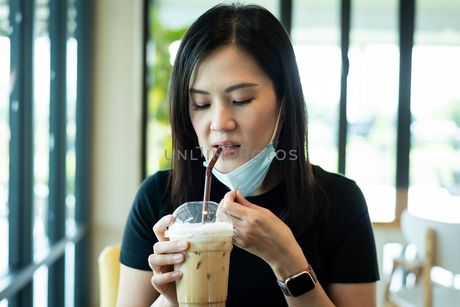 An Asian beautiful woman has to remove a blue mask and drinking an iced cappuccino with happiness in the morning.