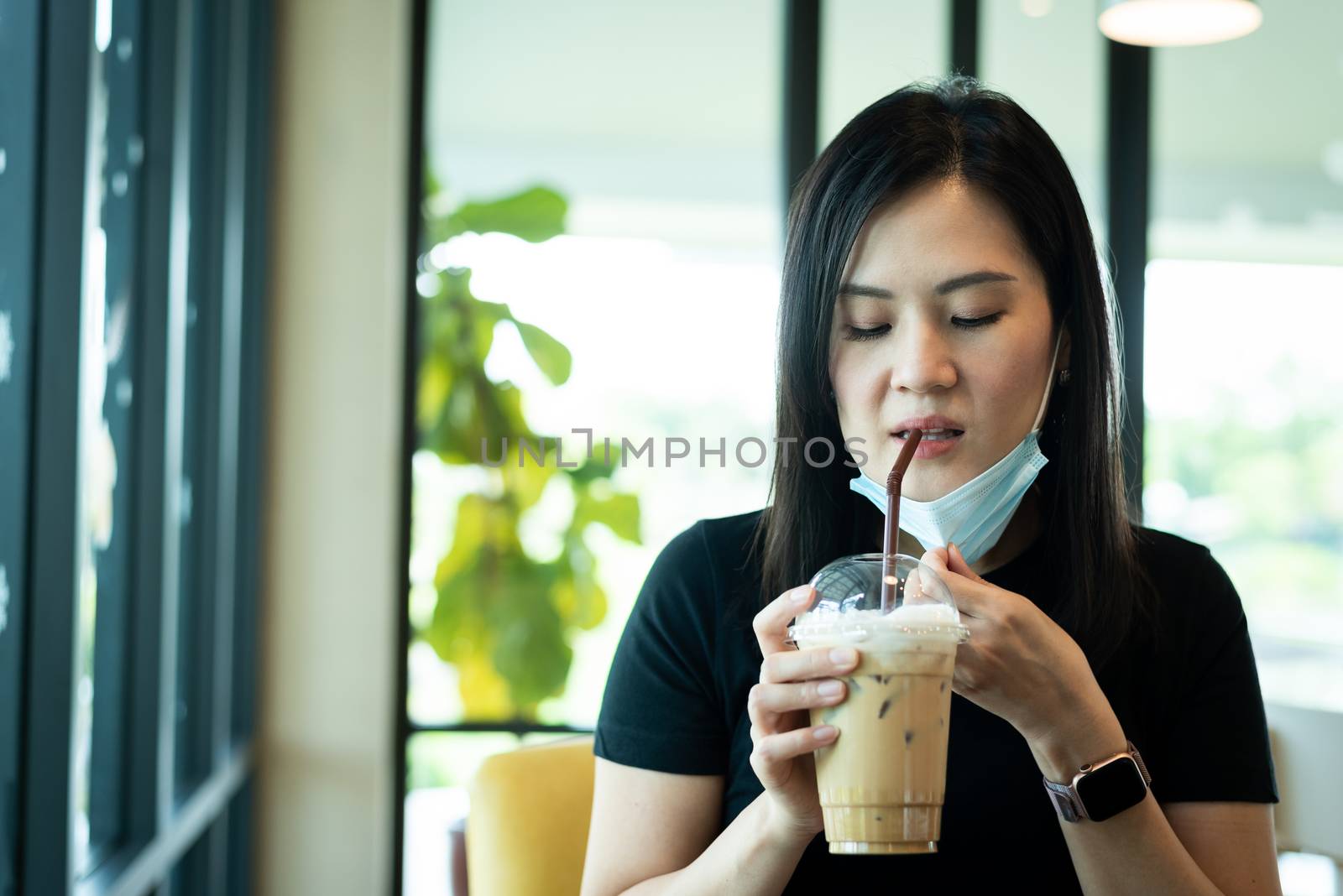 An Asian beautiful woman has to remove a blue mask and drinking an iced cappuccino with happiness in the morning.