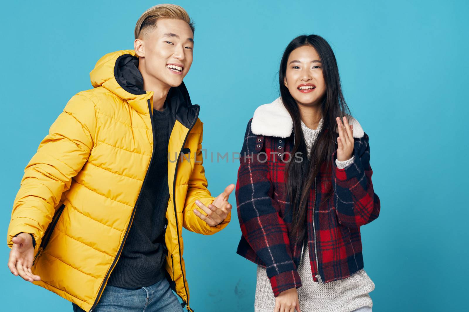 Cheerful young people on isolated background advertise warm clothes and laugh at the camera