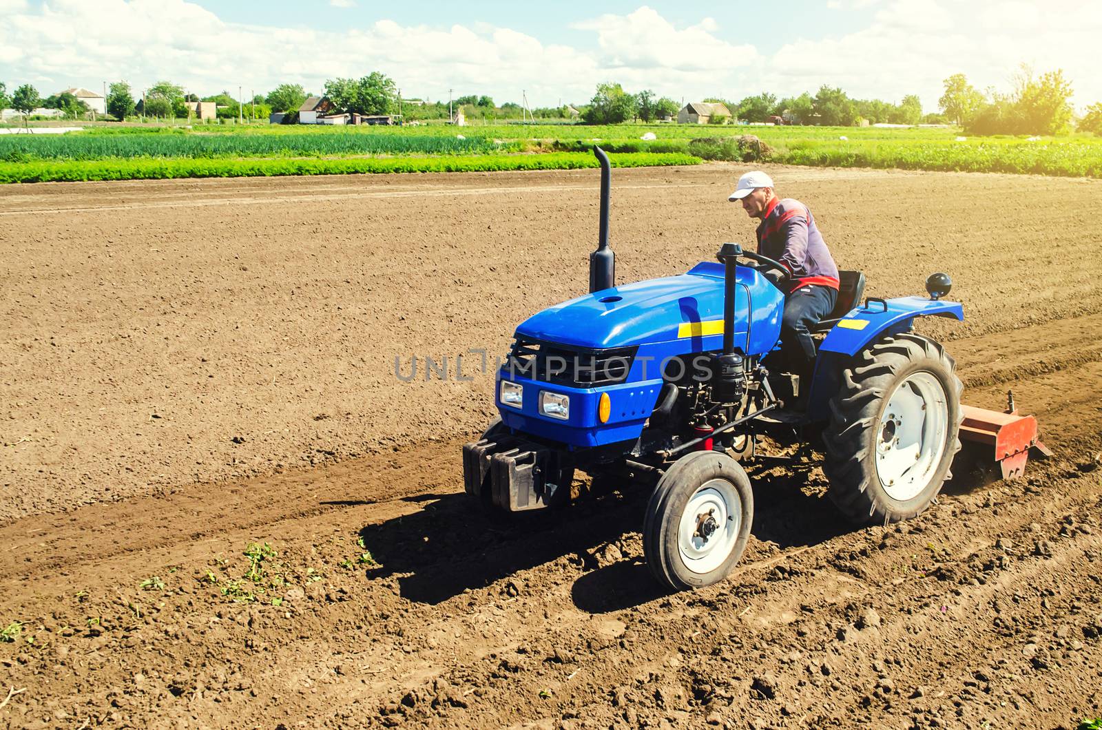 Farmer on a tractor with a milling machine processes loosens soil in the farm field. Grind and mix soil on plantation. Preparation for new crop planting. Loosening surface, cultivating the land. by iLixe48