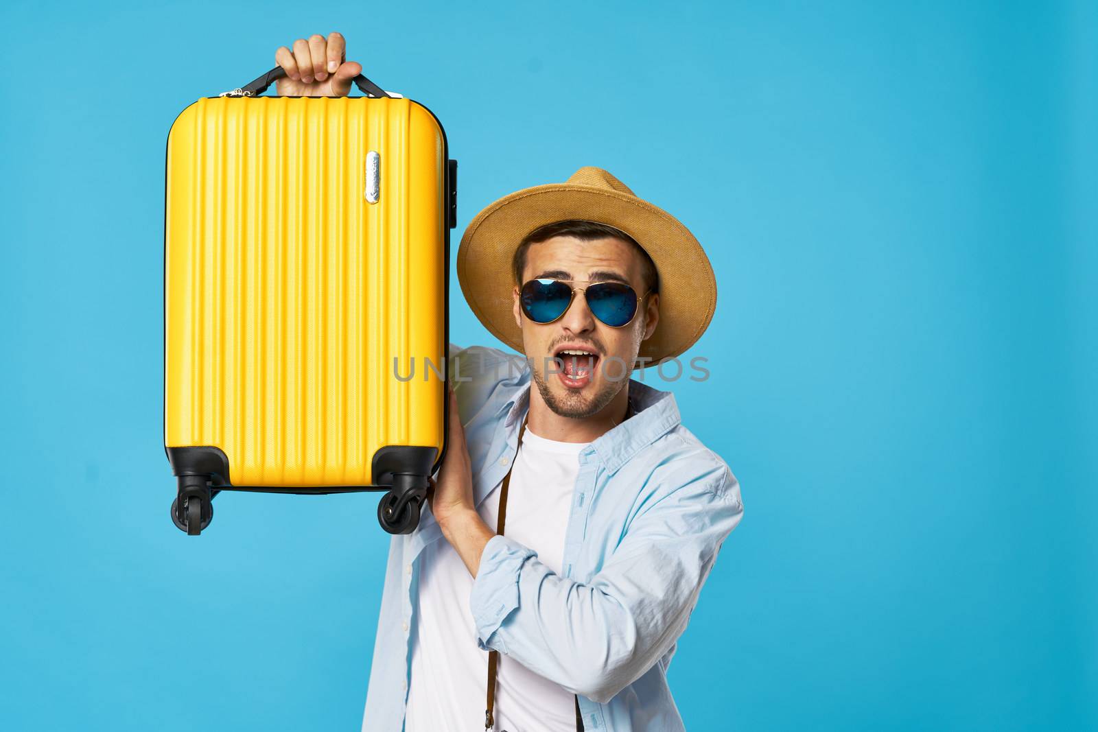 man on a blue background with glasses and a yellow suitcase in his hands