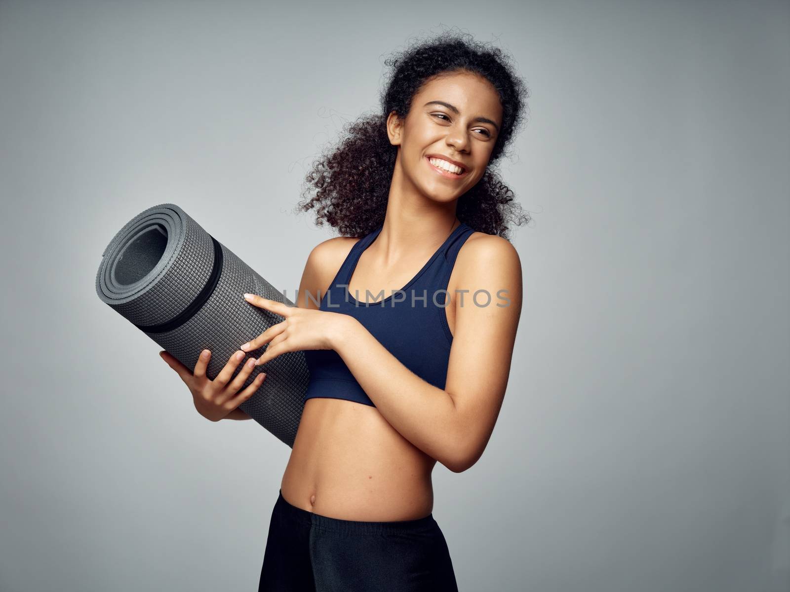 A sports woman in a short T-shirt and jeans holds a fitness mat in her hands