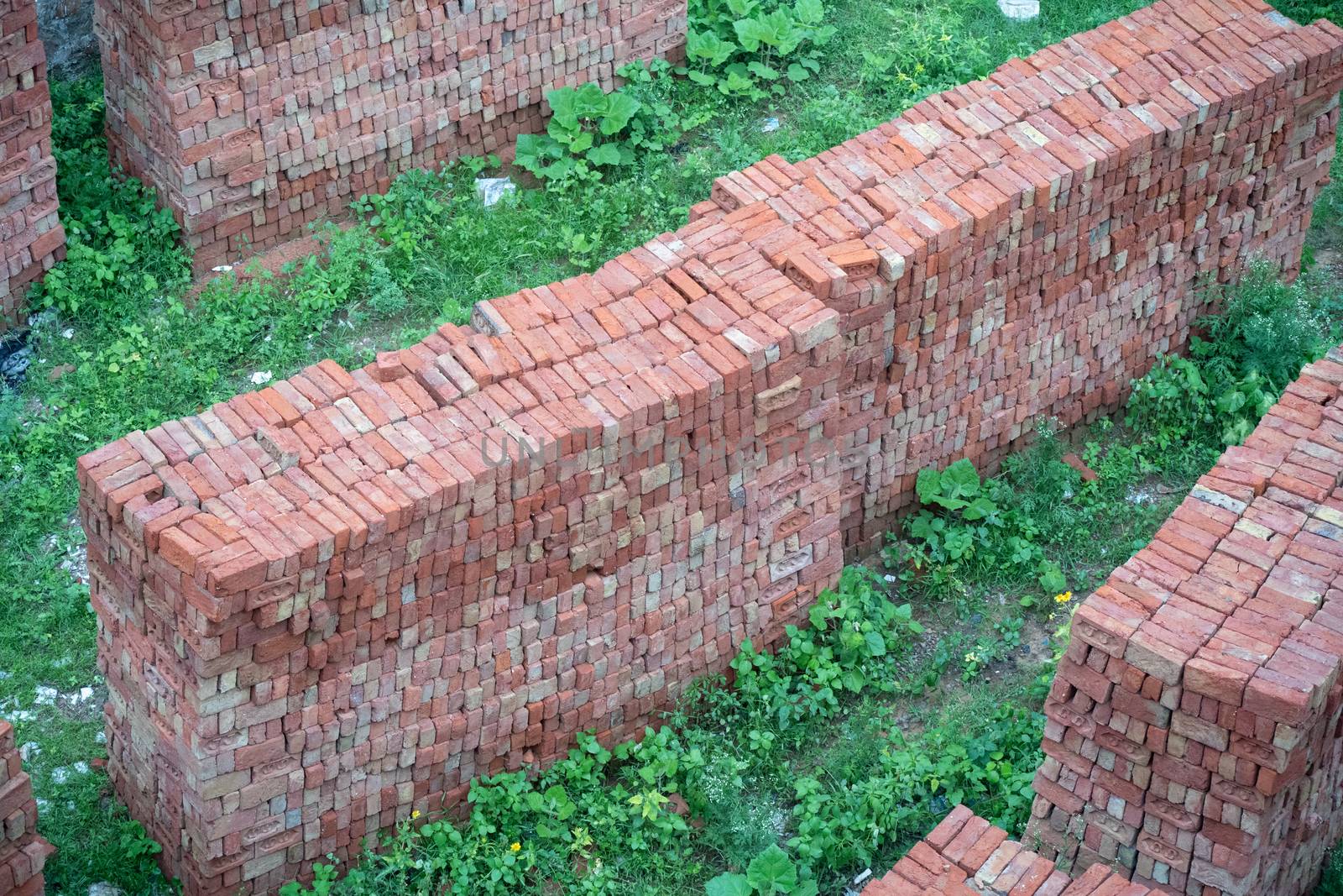 shot of bricks placed in high ordered piles on grass ready for t by Shalinimathur