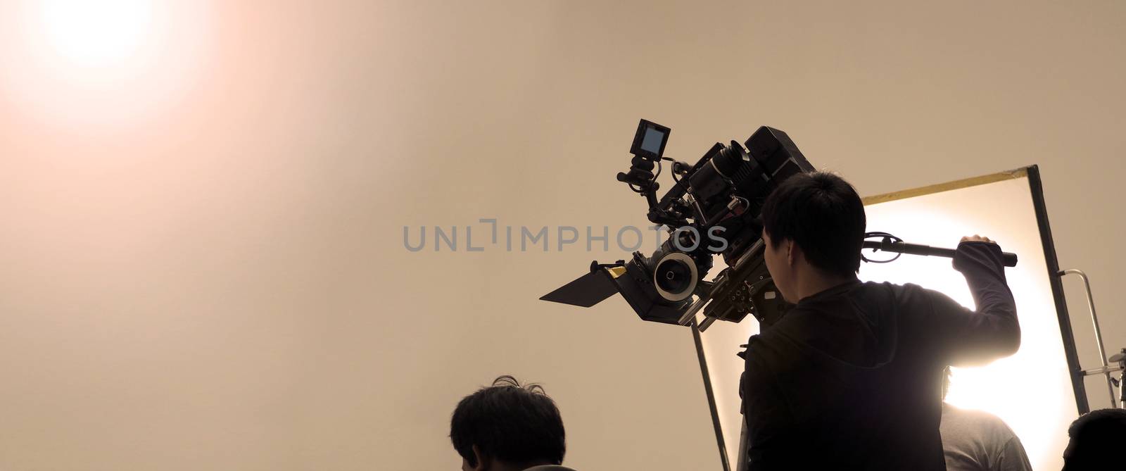 Behind the shooting or filming video movie and film production crew team setting up camera on tripod and professional equipment in studio for offline tv commercial or online web film recording.